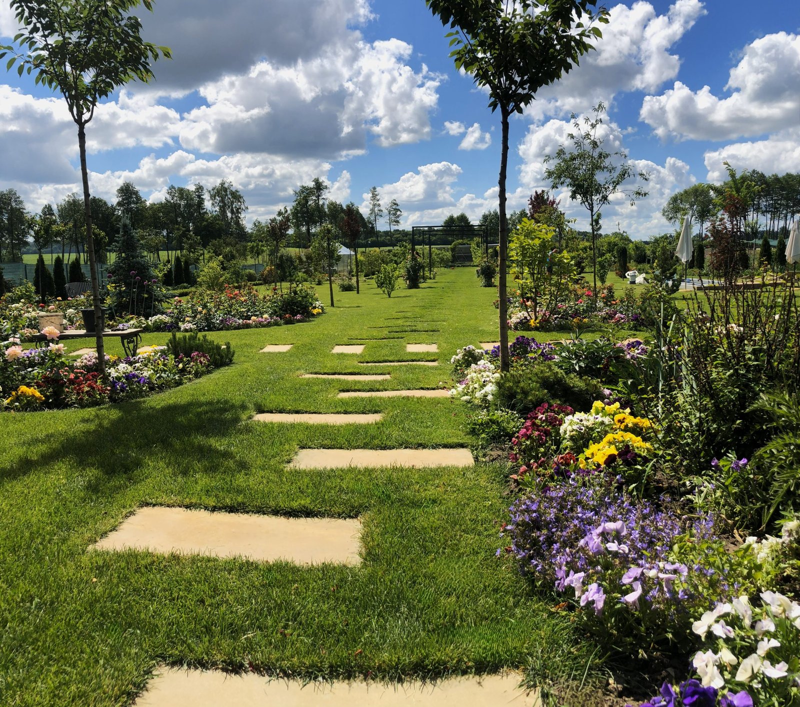 Beautiful landscaping featuring a pathway, sod, trees, and flowers.